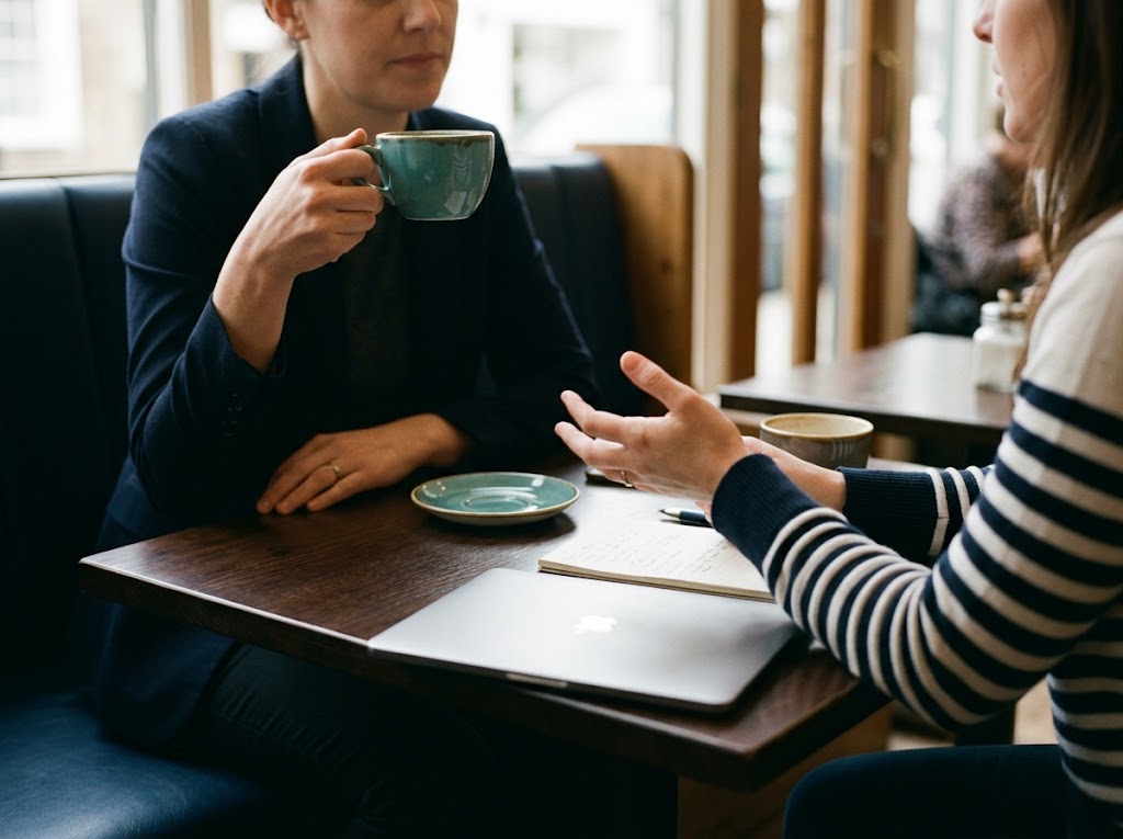 Two professionals in quiet conversation over a notepad and coffee, side-lit natural interior